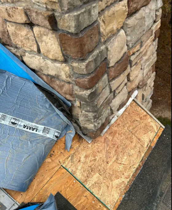 Exposed roof decking and flashing at the base of a stone chimney.