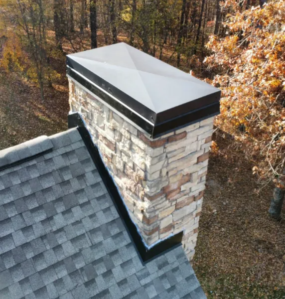 Metal cap on a stone chimney above a shingle roof.
