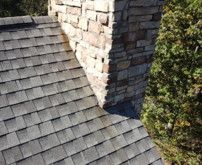 Stone chimney surrounded by asphalt roof shingles.